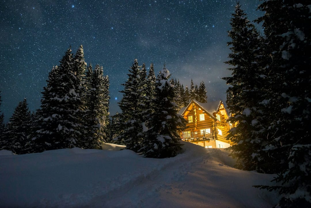 Beleuchtetes Holzchalet zwischen verschneiten Tannen bei Nacht