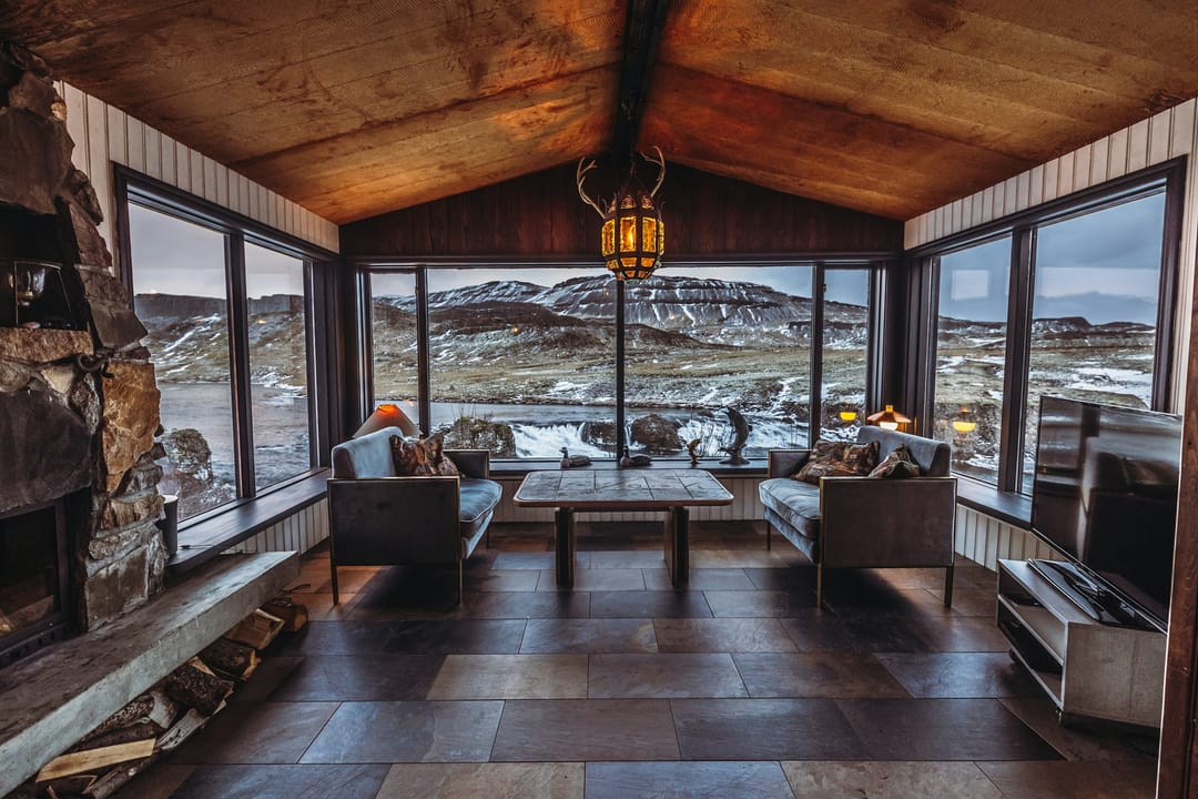 Wohnraum eines Chalets mit Kamin und grossen Fenstern zu den Bergen